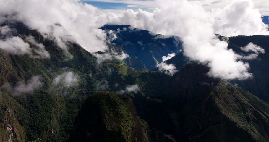 Wide panoramic drone view of Machu Picchu citadel surrounded by clouds and lush green mountains in Andes of Peru. Aerial