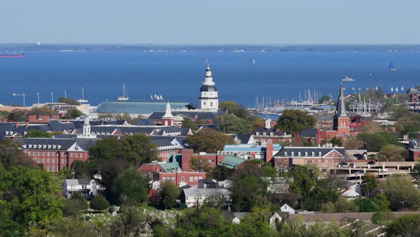 Wide aerial view of Annapolis, Maryland in spring sunshine with historic city skyline, church towers, marina boats and calm blue Chesapeake Bay waters in background. Panorama view.