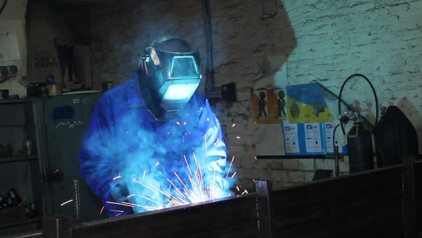 Male wearing uniform welds with welding machine torch
