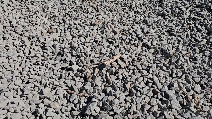 A large area covered with small stones and gravel is shown. The sun shines brightly in the clear sky. No other objects or plants are in view, creating a rugged landscape.