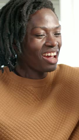Vertical video: Hearing voice, man in brown shirt near window laughing, showing white card leaving. Sweatshirt, dreadlocks, bracelets, tablet, gesture, candid, vertical video