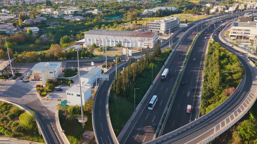 Beautiful aerial perspective of a modern multi-level road junction with cars and trucks driving along curved overpasses and ramps, surrounded by lush greenery and a sprawling cityscape