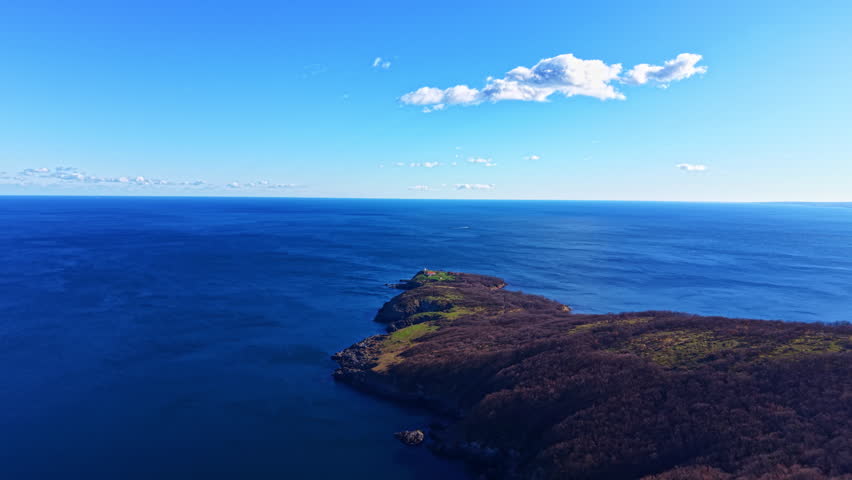 A wide view of the ocean with clear blue water and a small green island in the distance. Clouds are visible in the blue sky above.