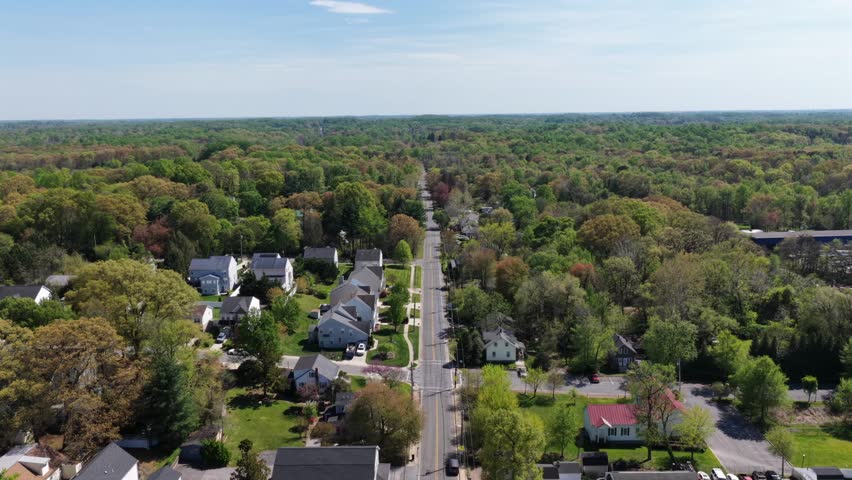Suburban Bowie Maryland with residential street, homes and colorful spring trees in warm sunlight. Peaceful neighborhood landscape showing quiet community life in USA. Aerial descend shot.