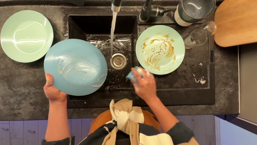 Student Quickly Rinsing And Scrubbing Green Plate With Soap And Water In Busy Kitchen Sink