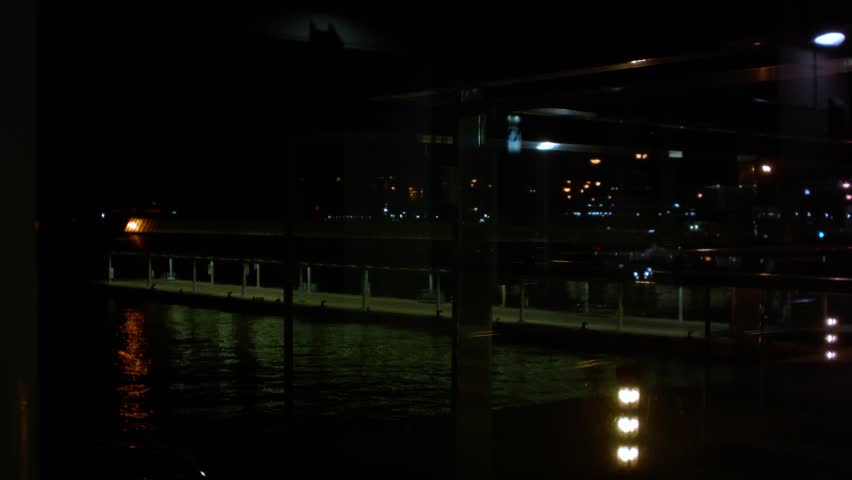 Night harbor through glass with illuminated docks reflecting on water