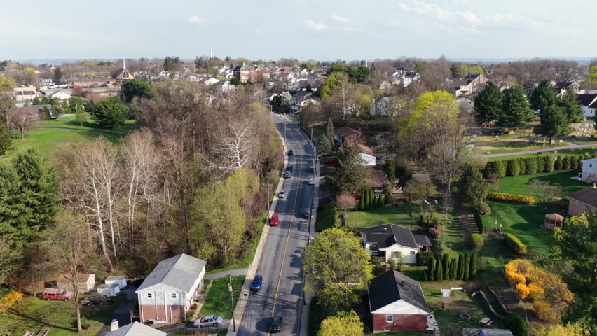 Aerial establishing shot of well kept suburb neighborhood during sunset time in America. Blooming trees in spring. Rising shot. Cars on Main Street. Wide shot. Pennsylvania, USA.