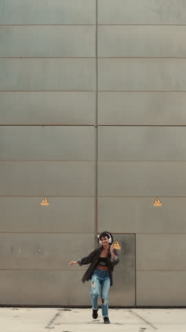 young woman dances enthusiastically, feeling beat and rhythm of music through headphones. Her movements full of energy and joy, set against urban backdrop and vibrant greenery.lost in music and moment