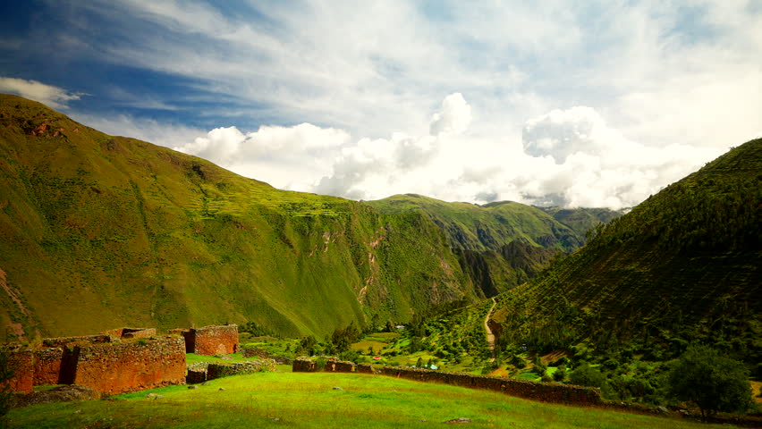 View of the ancient stone walls of the Pumamarca ruins overlooking the lush green landscape of the Sacred Valley in Peru under a cloudy sky
