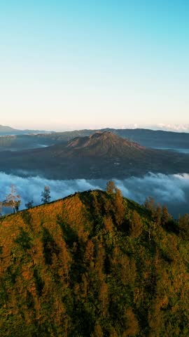 Bali mountain landscape with crater lake and volcanic terrain in golden light, low clouds and long shadows across the terrain. Vertical push-in drone footage