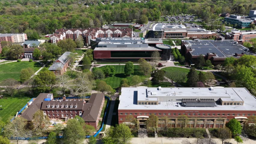 Bowie State University campus in sunny spring with modern academic buildings, green lawns and rooftop solar panels. Aerial lateral drone view of sustainable American college grounds. Wide shot.