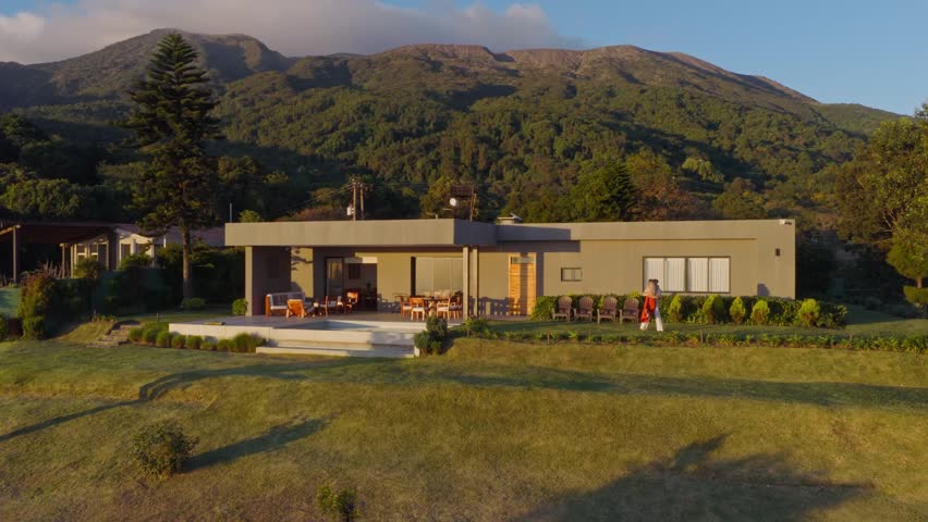 Couple walking in front of their Modern House in El Salvador, Surrounded by a Mountain Range and a Green Lawn