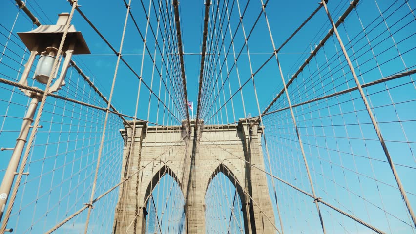 Low angle view of Brooklyn Bridge towers and cables, New York City landmark, architectural detail, urban transportation, sunny day, American symbol footage.