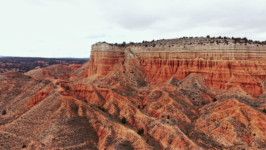 A canyon is visible with layers of rock showing different colors and patterns. The terrain is mostly dry, with some vegetation and a few trees scattered across the landscape.