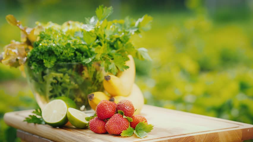 Serving colorful fruit and vegetable smoothies outdoors. Fresh ingredients like strawberries, bananas, and limes are visible. Healthy lifestyle and nutrition concept.