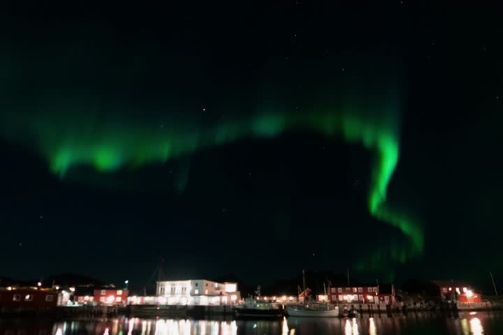 A stunning night view shows the Aurora Borealis (northern lights) phenomenon, a bright green arcing across the dark, starry sky.