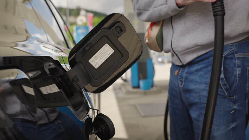 Man refueling black car at gas station with fuel cap showing E5 and E10 gasoline labels.