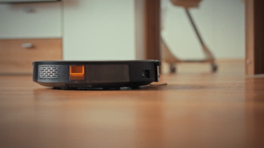 In a modern living room, an autonomous robot vacuum cleaner uses AI-driven sensors to map the floor, methodically cleaning the surface during daylight, demonstrating efficient smart-home technology