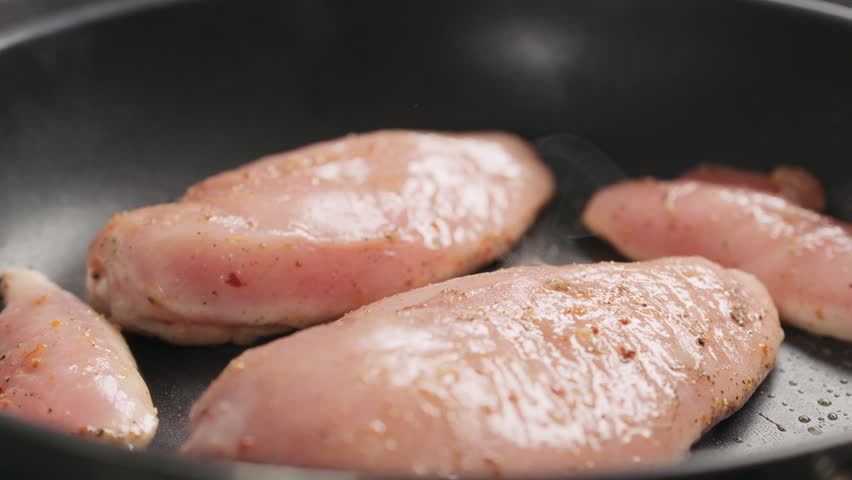 Slow motion man hand turn chicken fillet on non stick pan closeup