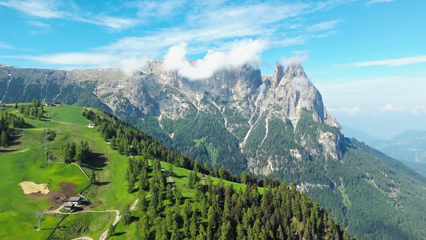 Rock cliffs of Dolomites above alpine meadows in Alpe di Siusi, South Tyrol, Italy. Aerial view with forest slopes and clear sky
