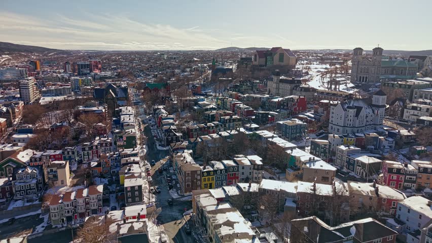 Wide aerial view of colorful jellybean row houses covering hillsides of downtown St Johns Newfoundland in winter with basilica visible in distance