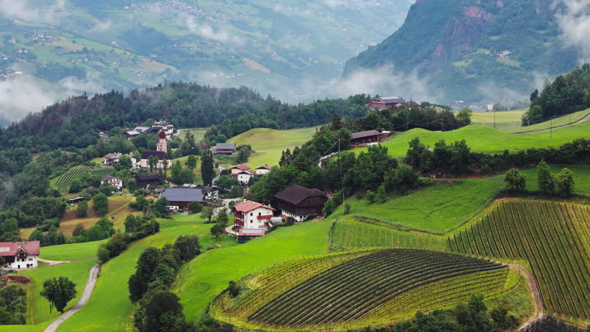 Alpine village with houses and vineyards on green hills in Dolomites, South Tyrol, Italy. Rural lifestyle in mountainous terrain