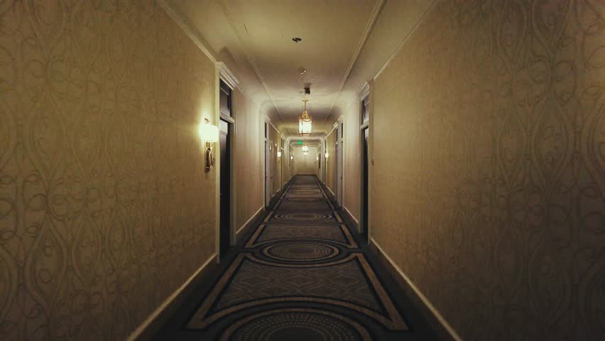 San Francisco. A long, dimly lit hallway with ornate wallpaper and a patterned carpet. The hallway leads to a light at the end of the corridor, with a series of doors on either side.