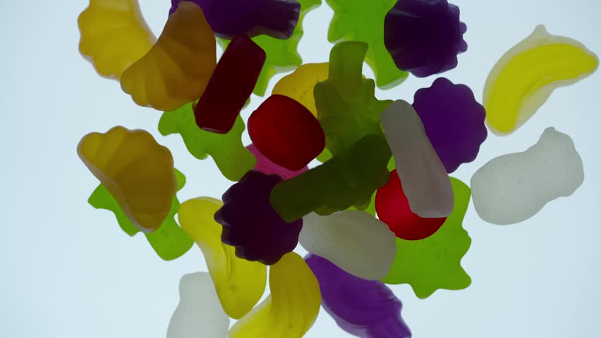 Colorful fruit shaped gummy candies being arranged with tweezers on a white background