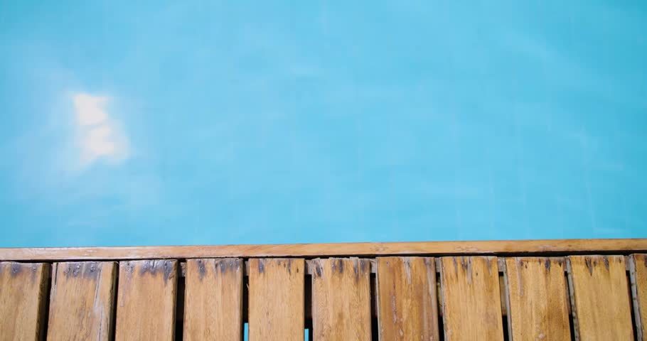 Slow motion footage front a side of a swimming pool showing a wooden walkway on a sunny day