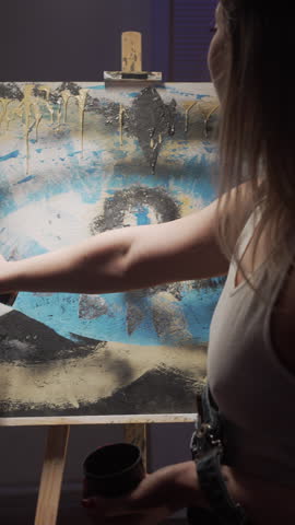 Female artist is painting picture with paint spray can spraying on canvas in her dark modern studio.