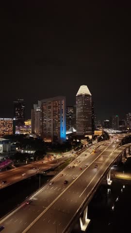 Singapore city highway at night with vehicle light trails and illuminated downtown skyline. Aerial drone footage of urban traffic and infrastructure in the Asian metropolis. Vertical 4K aerial drone footage.