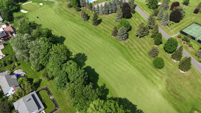 A country club sitting amidst a beautifully well-manicured lawn as fairways and forest surround it.