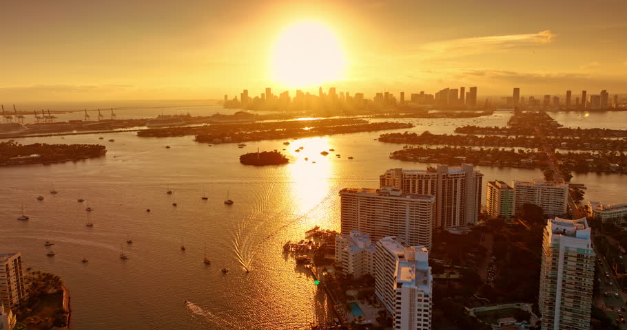Golden hour over the stunning Biscayne Bay. Flight over the waterscape with numerous vessels on. Approaching the skyline silhouette of Miami, Florida, USA.