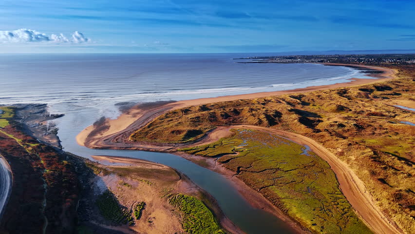Seashore with narrow line of sandy beach. Some water flows into the canal. Car rides by the highway at the rock. Aerial view.