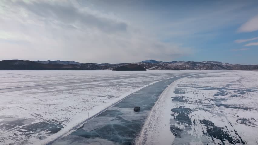 Drone footage of a vehicle driving along a cleared ice road across frozen Lake Baikal in winter, with snow patterns, blue ice and distant mountains, Russia