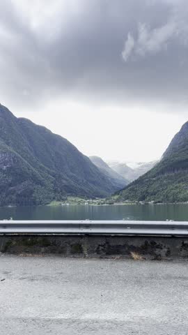 Roadside view of a wide fjord and layered mountain ridges filmed from a car.