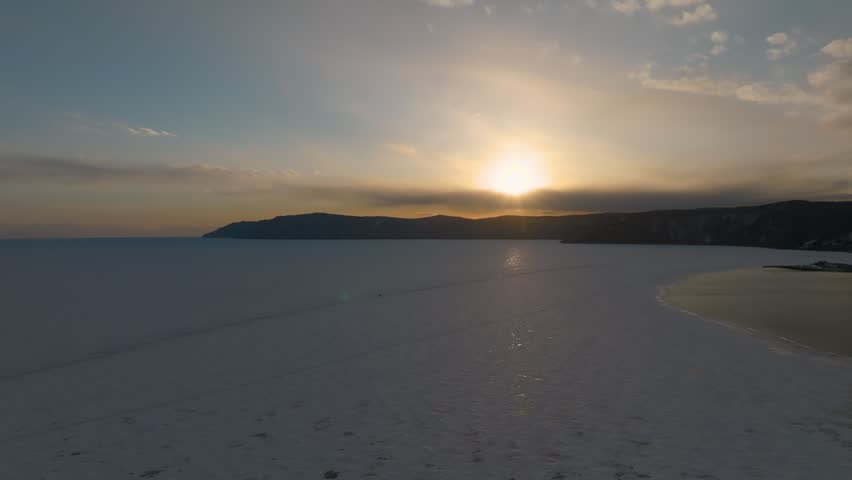 Aerial footage of winter sunset over frozen Lake Baikal near Listvyanka, where the Angara River flows out, Irkutsk Oblast, Russia, calm sky and icy shoreline