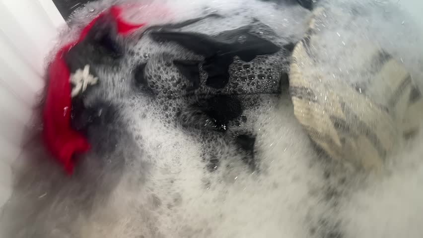 Close up top view of laundry washing in a machine with soap suds