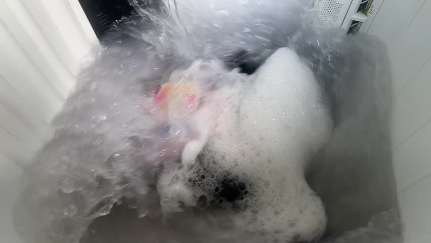 Close up top view of laundry washing in a machine with soap suds
