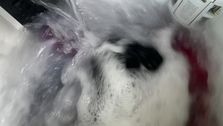 Close up top view of laundry washing in a machine with soap suds