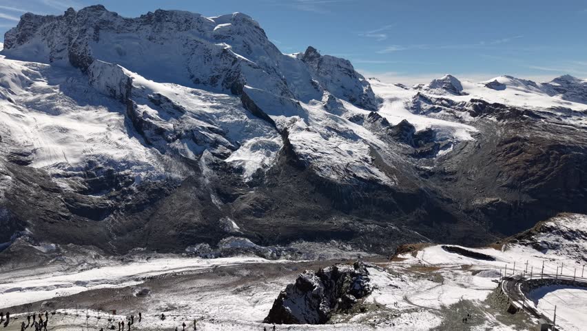 Aerial flyover next to the observatory of Gornergrat in Zermatt, Switzerland with a view of the train station and Dufourspitze mountain peaks a snowy autumn day in the Swiss Alps
