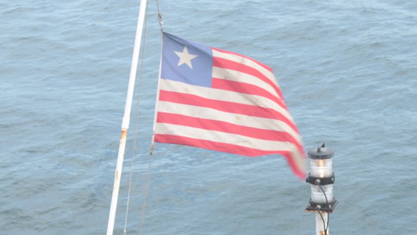 liberian ship registration flag fluttering on ensign pole at the poop deck of a cargo vessel with aft anchor light and open sea in the background