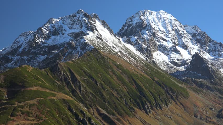 Majestic Alps mountains rise with snow covered peaks and dramatic alpine slopes under clear sky. Iconic european summits dominate bright lofty ridges, travel scenery, grandeur stock search appeal. The Alps are Europe’s highest mountain system, and the snow peaks, ridgelines, clear sky, alpine slopes, and lofty scale add strong travel, geography, and wilderness relevance.
