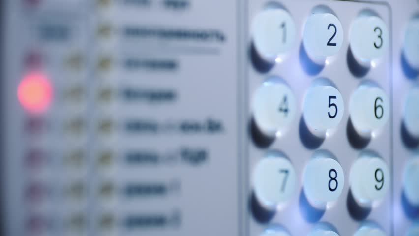 Close up shot of human finger pressing number two key on white electronic security keypad system with illuminated buttons and blurry signal light indicating arming sequence in indoor residential setting.