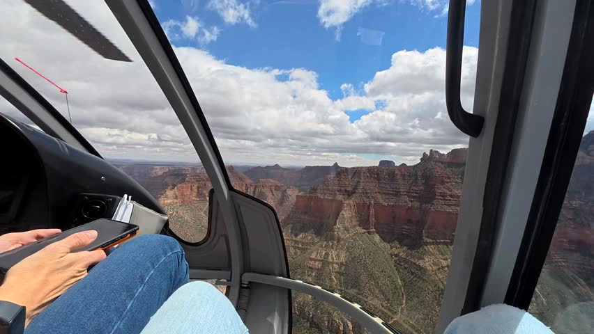 Pov view from inside a helicopter flying above the majestic grand canyon, with a passenger taking pictures with a smartphone of the breathtaking red rock formations and canyons in arizona