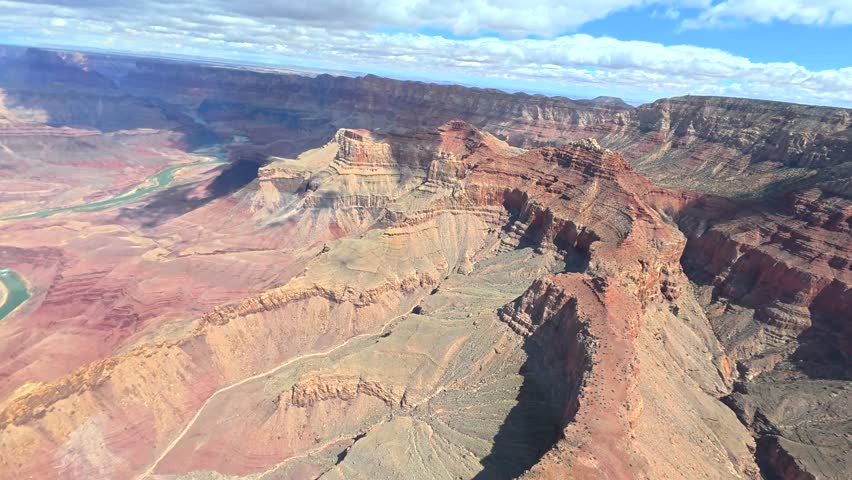 Point of view from a helicopter flying over the breathtaking landscape of the grand canyon national park, showing the colorado river snaking through the immense red rock formations below
