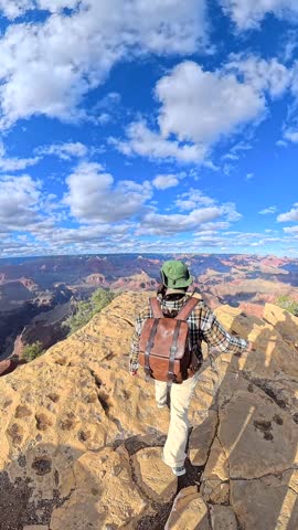 Brave female hiker with a backpack walking along a narrow, rocky ridge to a viewpoint, admiring the stunning panoramic vista of the grand canyon national park on a sunny day in arizona