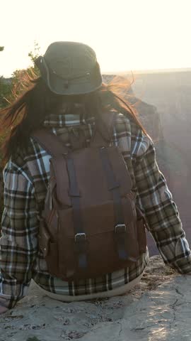 Beautiful young woman sitting on a rock at the edge of a cliff, admiring the stunning panorama of the grand canyon national park with the colorado river in the background