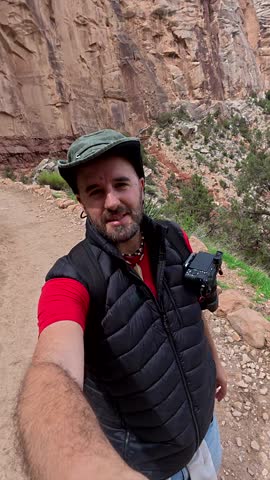 Cheerful male traveler and vlogger recording a selfie video while hiking along the bright angel trail in grand canyon national park, sharing his solo adventure and the stunning scenery