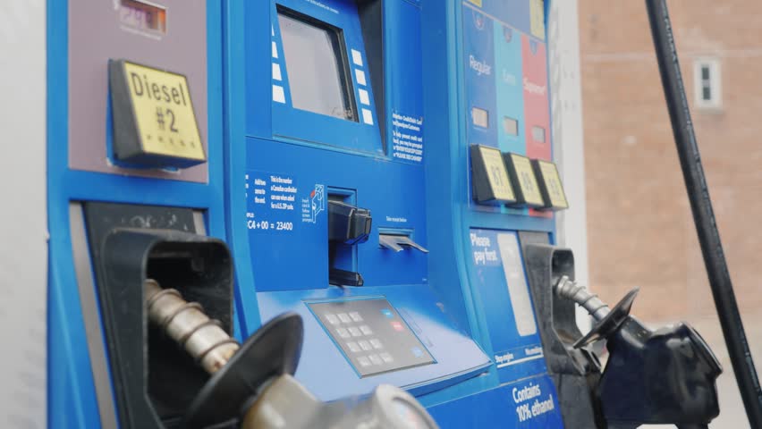 Footage shows hand swiping credit card into machine. Person presses buttons on keypad and selects regular fuel grade at outdoor filling station. Close up shot of gas pump transaction process.